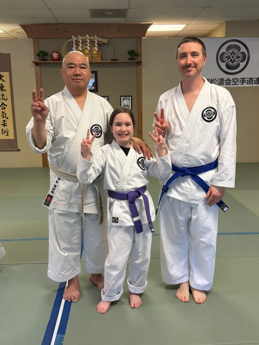 Two adult karateka standing with a smiling young student