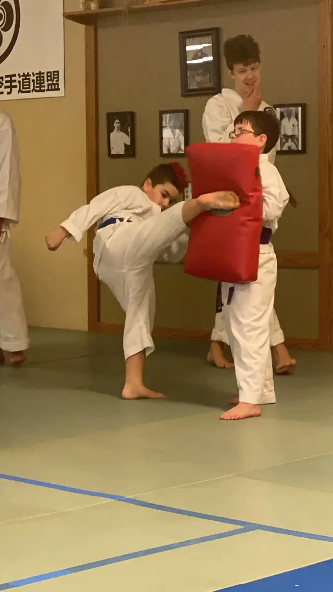 Young karate student practicing a side kick against a red training pad